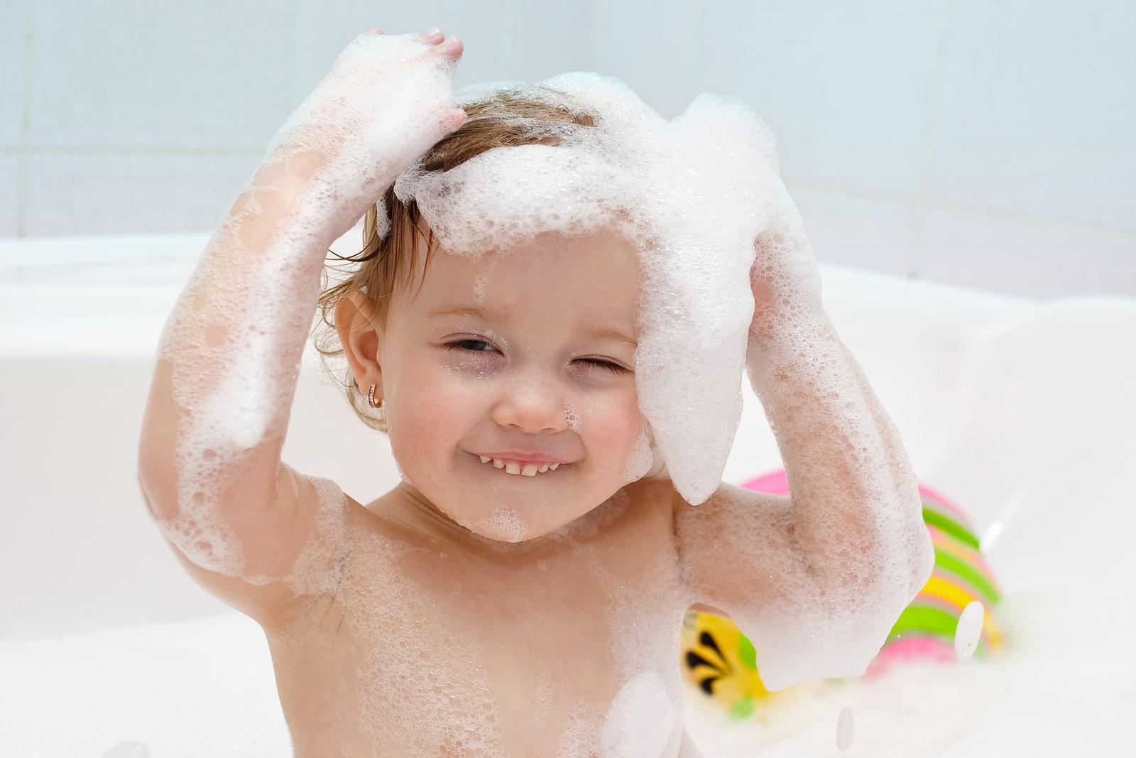 Ein Kleinkind in der Wanne lacht und hat Shampoo-Schaum auf den Haaren 